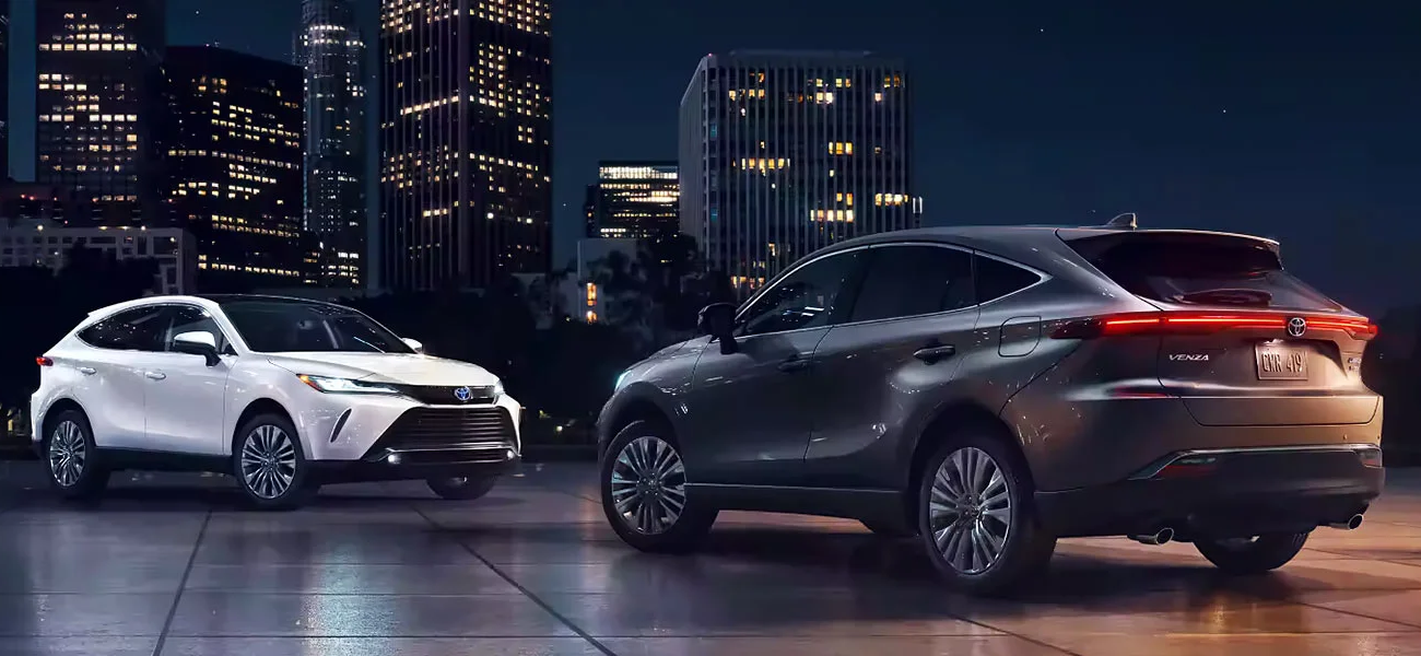 Two different 2024 Toyota Venza models sitting in a dark parking lot against a city skyline backdrop